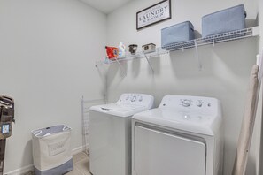 A laundry room with two front-loading washing machines, a drying rack, and a shelf with laundry supplies. - Private Community w/ Pool, Near Gulf Beaches (Palmetto)