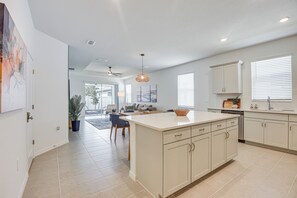 A modern kitchen with a central island, white cabinetry, and a dining area with a view to the outdoors. - Private Community w/ Pool, Near Gulf Beaches (Palmetto)