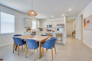 A modern kitchen with white cabinets, a central island, and blue chairs around a wooden dining table. - Private Community w/ Pool, Near Gulf Beaches (Palmetto)