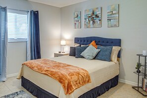 A bedroom with a bed, a nightstand, a lamp, a window with curtains, and artwork on the wall.