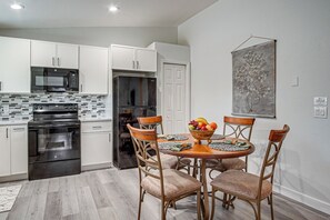 A modern kitchen with white cabinets, a black refrigerator, and a microwave. There is a dining table with four chairs and a fruit bowl on it.