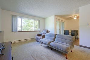 A spacious living room with a large window, a sofa, a chair, and a dining area with chairs. - 12 Mi to JBLM: Olympia-Area Escape (Lacey)