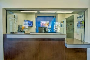 A reception desk with a computer, a monitor, and a blue wall with informational posters. - 1 Queen Bed | ADA/Tub (PHOENIX)