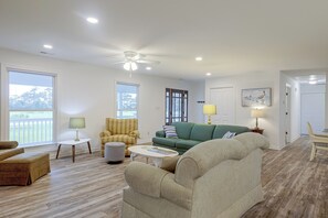 Ein geräumiges Wohnzimmer mit Deckenventilator, großen Fenstern und Blick auf eine Terrasse.