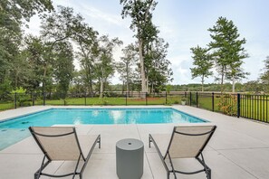 A rectangular swimming pool with two lounge chairs facing it, surrounded by a black metal fence, and trees in the background. - Pool & Hot Tub at Gated Waverly Home (Waverly)