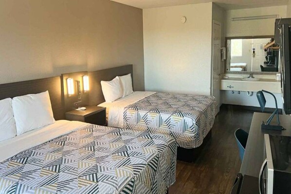 A hotel room with two beds, a nightstand, a desk with a chair, and a bathroom visible through an open door.