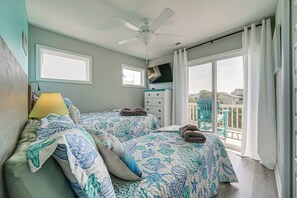 Ein Schlafzimmer mit zwei Betten, einem Deckenventilator, einem Fernseher und einem Balkon mit Blick.