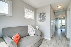 En moderne stue med en grå sofa, en dekorativ vægkunst og udsigt til det tilstødende soveværelse.