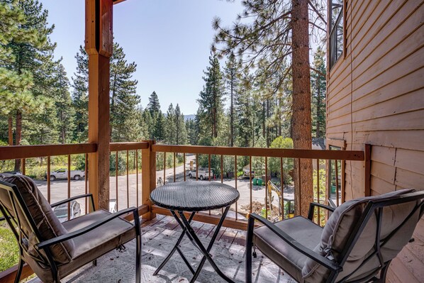 A wooden deck with two chairs and a small table, overlooking a forested area and a road. - Incline Village Condo Near Lake Tahoe Adventures (Incline Village)
