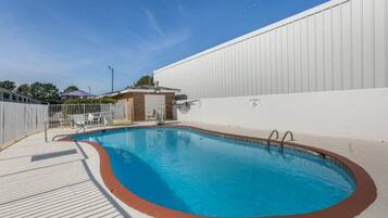 A swimming pool with a small adjacent structure, a fenced area, and a clear sky.