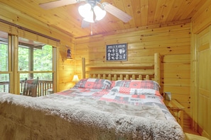 Een slaapkamer in een houten chalet met een bed, een plafondventilator, een raam en een bord waarop dieren uit het bos staan afgebeeld.