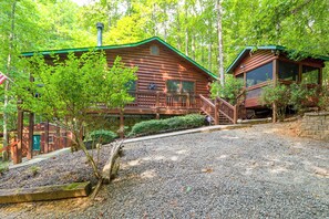 Une cabane en bois avec un porche, entourée d’arbres et de gravier.