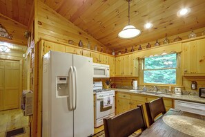 A wooden cabin kitchen with a refrigerator, stove, microwave, and a window overlooking greenery. - Pet-Friendly Cozy Cabin Retreat  Hot Tub & Trails (Cherry Log)