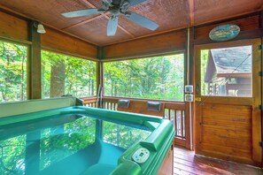 Une cabane en bois dotée d’un bain à remous, de grandes fenêtres et d’une porte sur laquelle est apposée une pancarte.