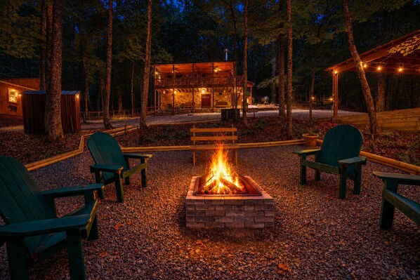 Une cabane avec un foyer, entourée de fauteuils Adirondack, située dans une zone boisée.