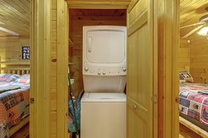 A compact room with a washing machine, a bed with a patterned blanket, and a sign listing animals of the lodge. - Pet-Friendly Cozy Cabin Retreat  Hot Tub & Trails (Cherry Log)