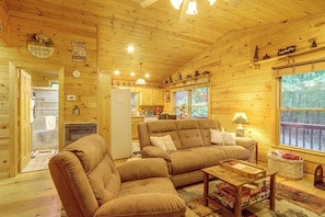 A cabin interior with a sofa, a dining table, and a kitchen area. - Pet-Friendly Cozy Cabin Retreat  Hot Tub & Trails (Cherry Log)