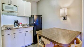 A compact kitchen with a microwave, refrigerator, coffee maker, and a wooden table with chairs.