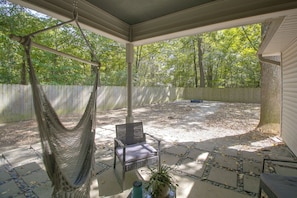 A covered patio with a hammock, a chair, and a potted plant.
