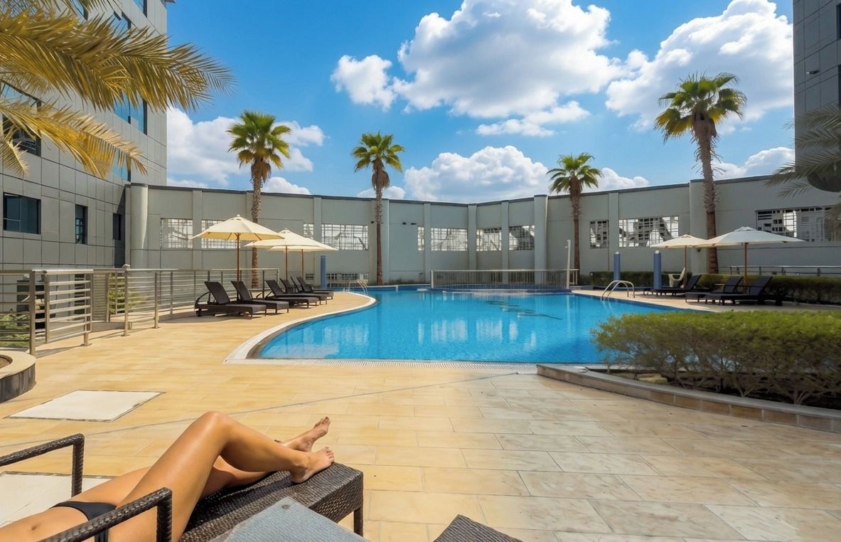 A pool area with lounge chairs and umbrellas, surrounded by palm trees and a building.
