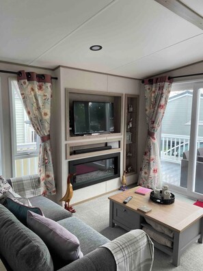 A living room with a flat-screen TV, fireplace, sofa, and a table with a remote control. - Charming Tattershall Mobile Home 3 Bedrooms, Private Entrance, Shared Pool (Tattershall)