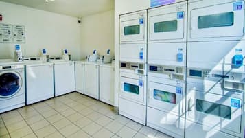 Een wasserette met meerdere wasmachines en drogers, een betegelde vloer en een bord waarop staat dat men geen verantwoordelijkheid neemt voor onbeheerde spullen.