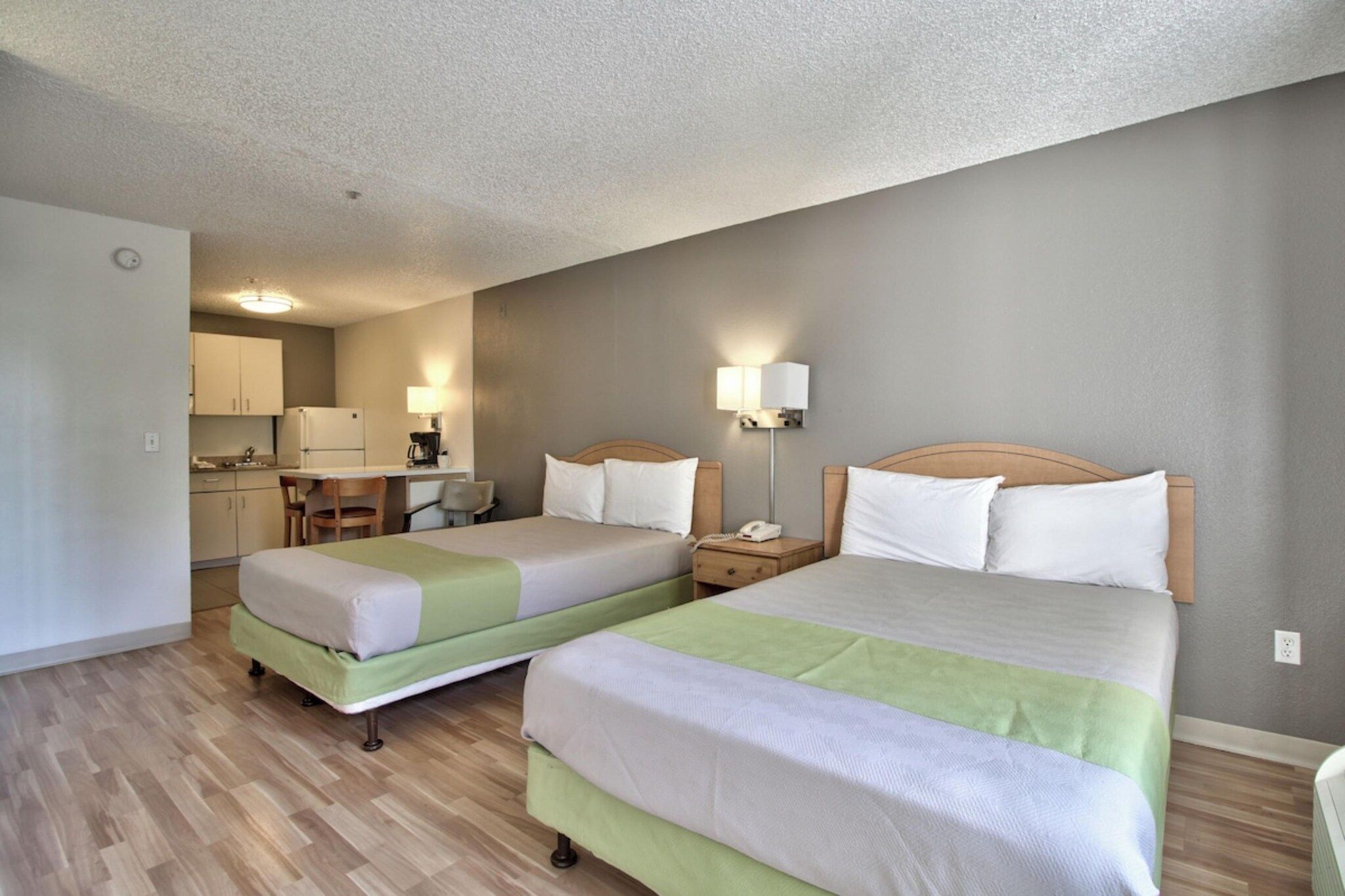 A hotel room with two beds, a kitchenette, and a bathroom.