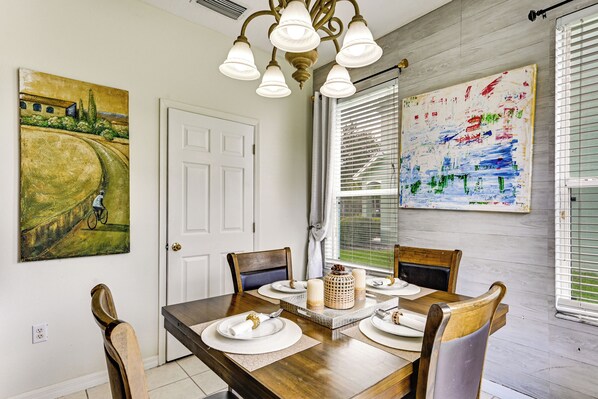 A dining area with a wooden table set for four, a chandelier, and artwork on the walls. - Pool Access! Steps from Upper Tampa Bay Trail (Tampa)
