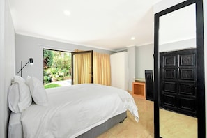 A bedroom with a bed, a desk, and a view of a garden.