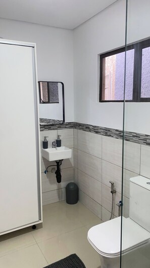 Uma casa de banho pequena e limpa, com sanita, lavatório e chuveiro.