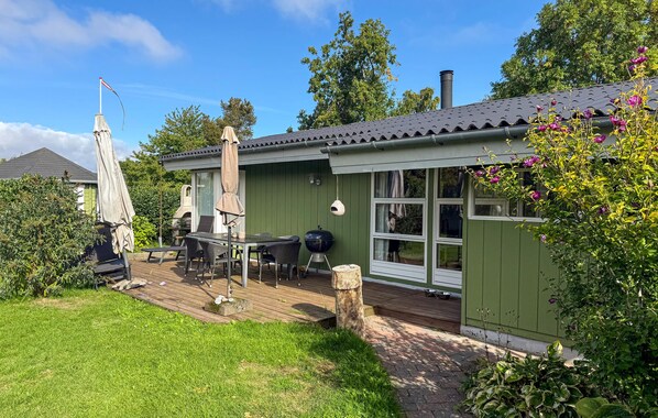 Ein grünes Haus mit Terrasse, Gartenmöbeln und Grill.