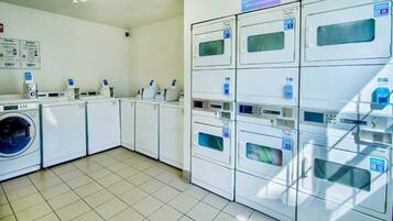 A laundry facility with multiple washing machines and dryers, a tiled floor, and a sign indicating the area is not responsible for unattended items.