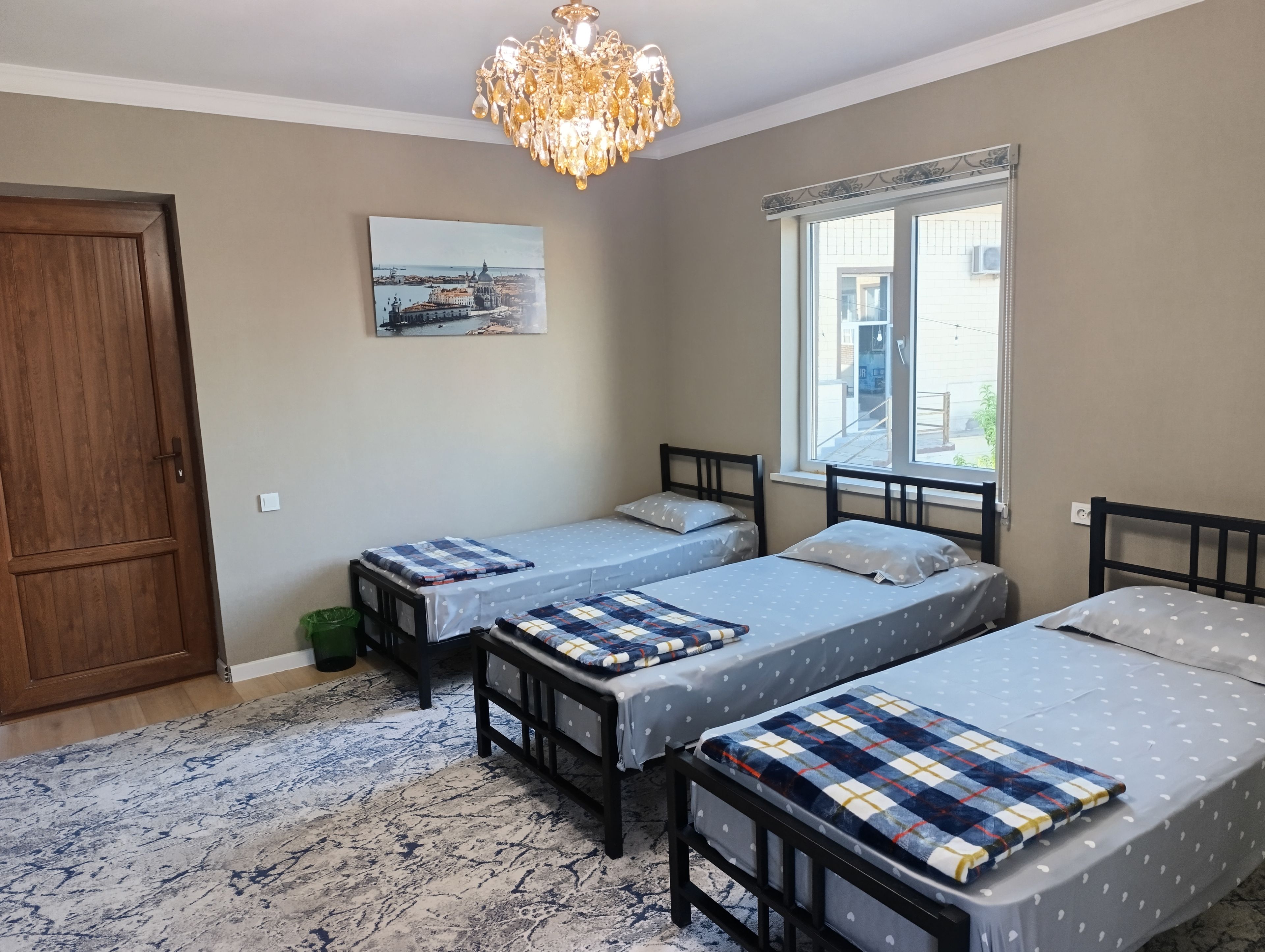 Quarto com duas camas, um candelabro, uma janela com persianas e uma porta.