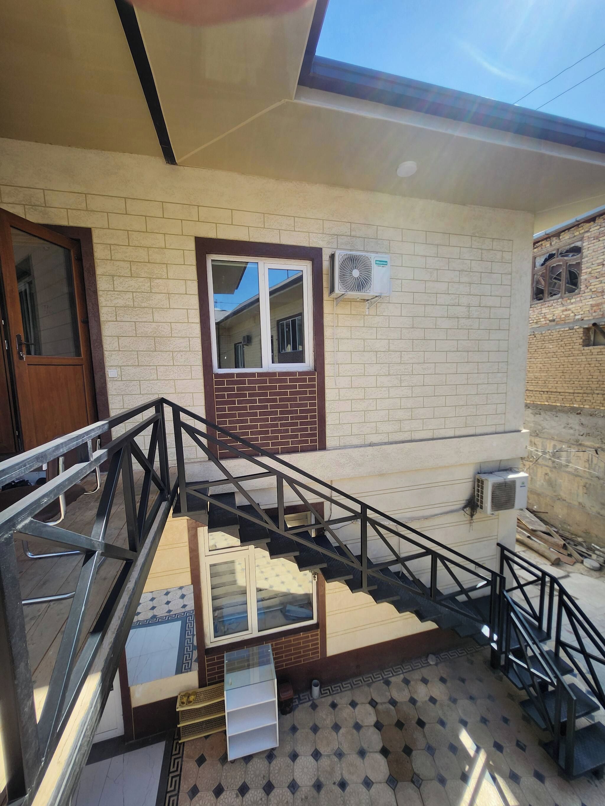 A staircase leading to a second-floor landing with a glass door, a window with a view, and an air conditioning unit on the wall.