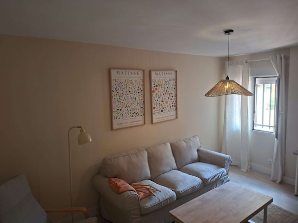 Un salon comprenant un canapé, une table basse, un lampadaire et deux œuvres d’art encadrées accrochées au mur.