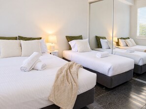 Ein Hotelzimmer mit zwei Betten, jeweils mit weißen Leinen und Kissen, einer Nachttischlampe und einem großen Spiegel, der den Raum widerspiegelt.