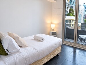 Ein Hotelzimmer mit Bett, Nachttisch mit Lampe und Blick auf die Stadt durch ein großes Fenster.