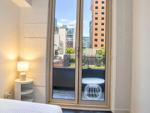 A hotel room with a bed, a bedside lamp, a small table, and a view of the city through a glass door. - Little Bourke City Charm (Melbourne)