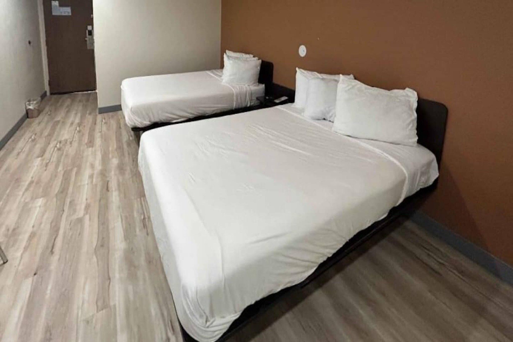 Une chambre d’hôtel avec deux lits simples, un plancher en bois et un mur uni.