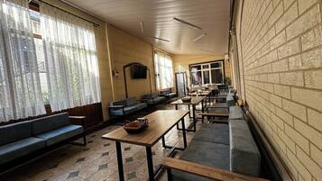 A long corridor with benches and tables, large windows with curtains, and a brick wall on one side.