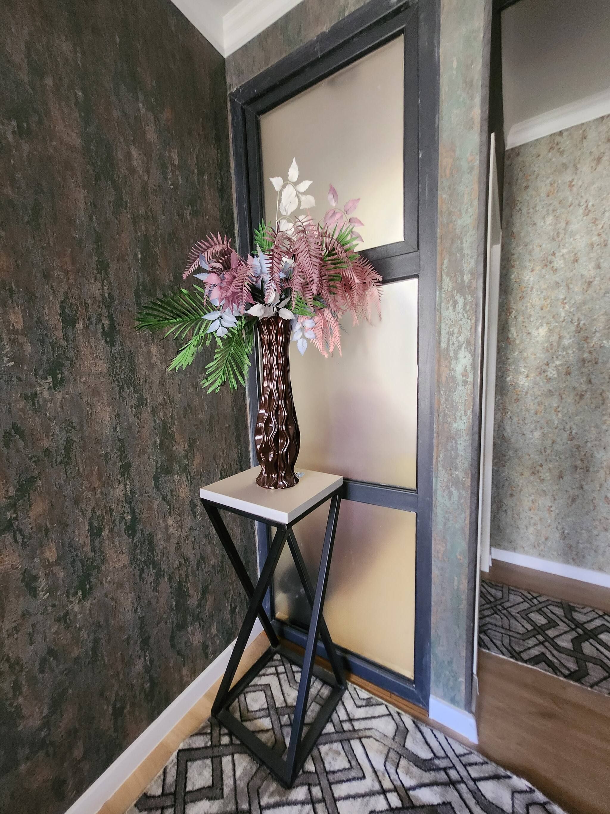A room with a decorative vase on a small table, a patterned carpet, and a textured wall.