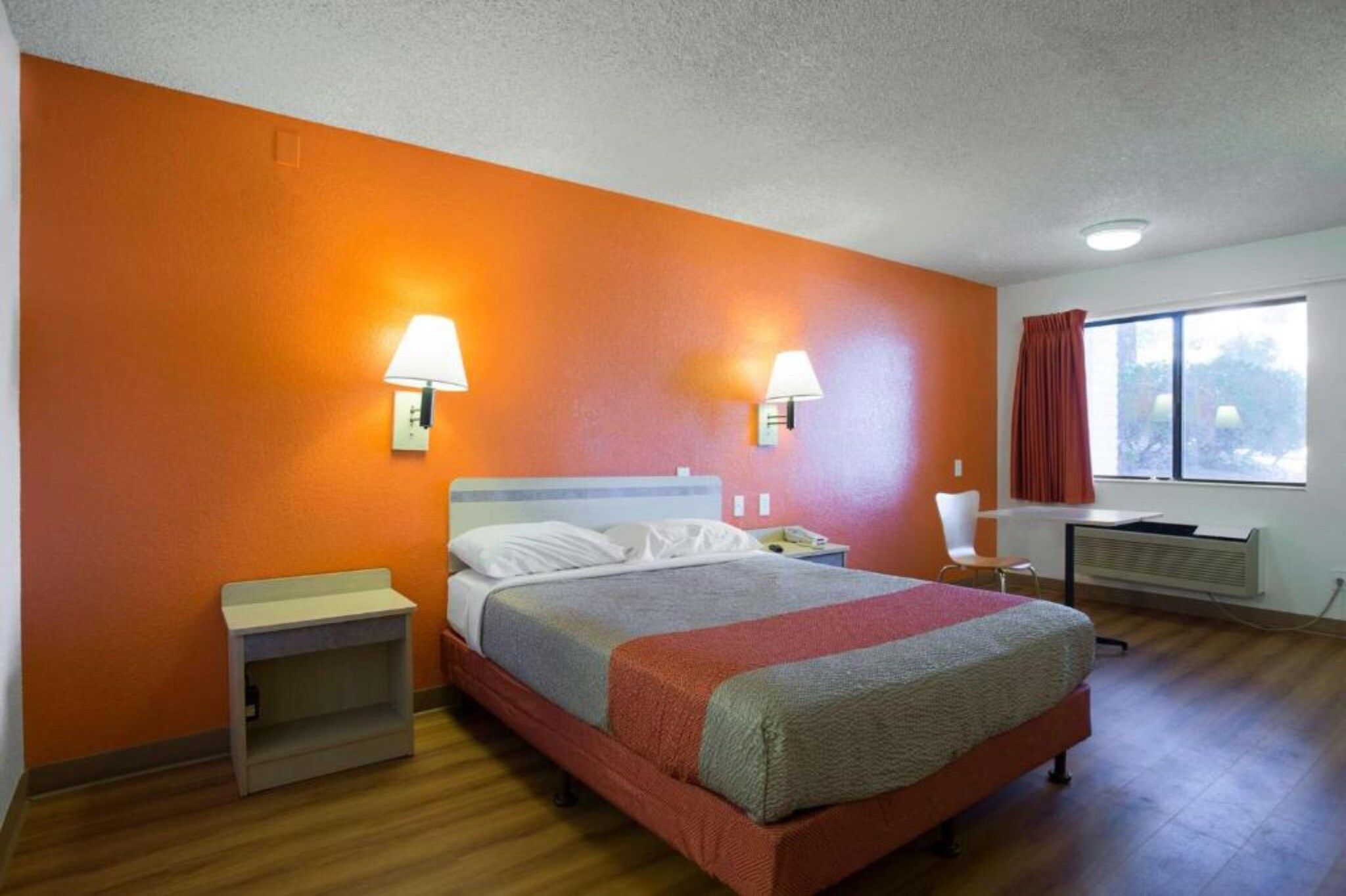 A hotel room with a bed, bedside tables, a desk, and a window with curtains.