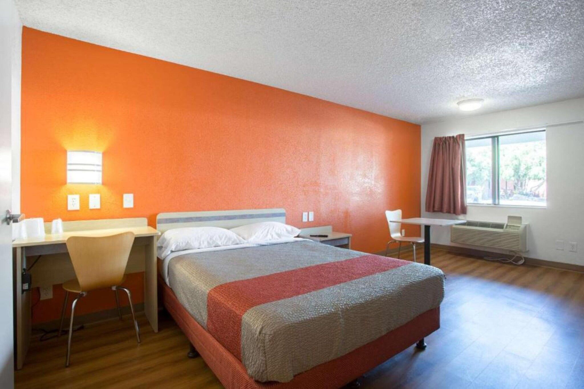 Ein Hotelzimmer mit Bett, Schreibtisch, Stuhl und einem fensterbepflanzten Fenster.