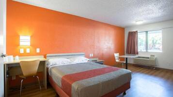 Ein Hotelzimmer mit Bett, Schreibtisch, Stuhl und einem fensterbepflanzten Fenster.