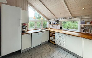 Eine Küche mit Holzbalkendecke, weißen Schränken, einem Geschirrspüler und einem Fenster mit Blick auf Grünflächen.