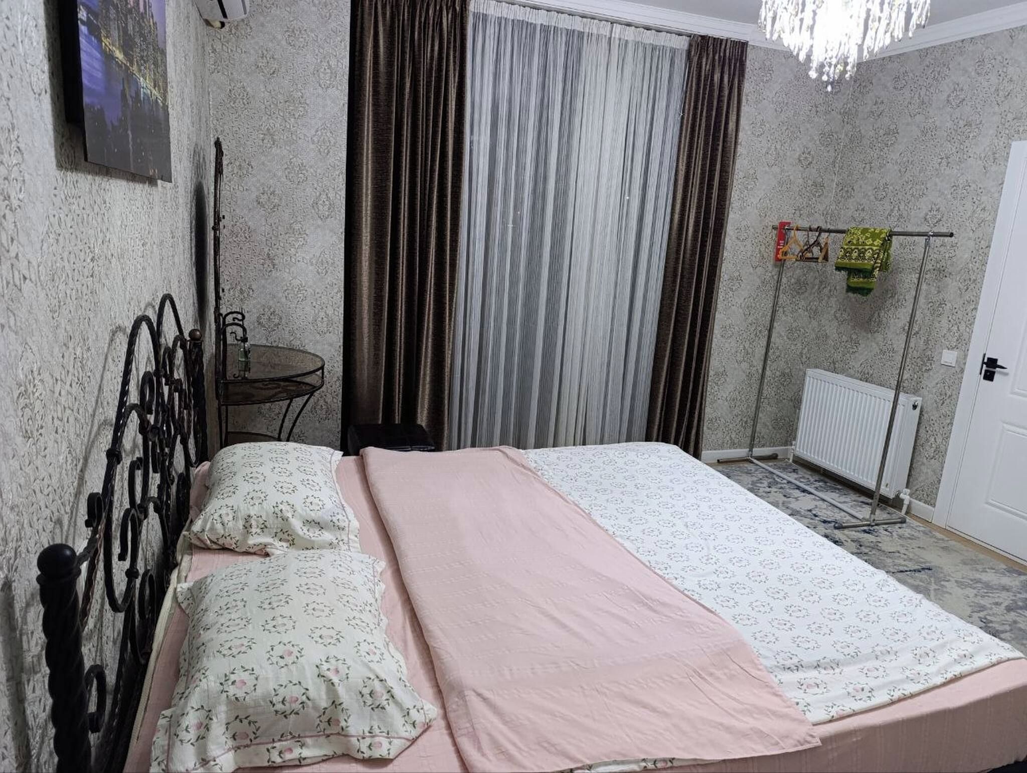 A bedroom with a bed, a small table, a radiator, and curtains.