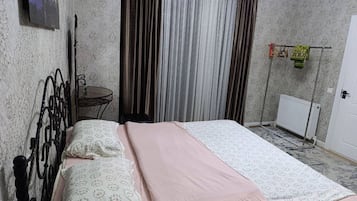 A bedroom with a bed, a small table, a radiator, and curtains.