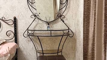 A room with a bed, a vanity with a mirror, and a small stool.