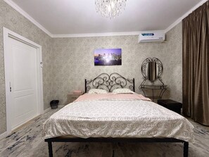 A bedroom with a bed, a nightstand, a wall-mounted air conditioner, a decorative mirror, and a door. - Nice room for family and couples (Tashkent)