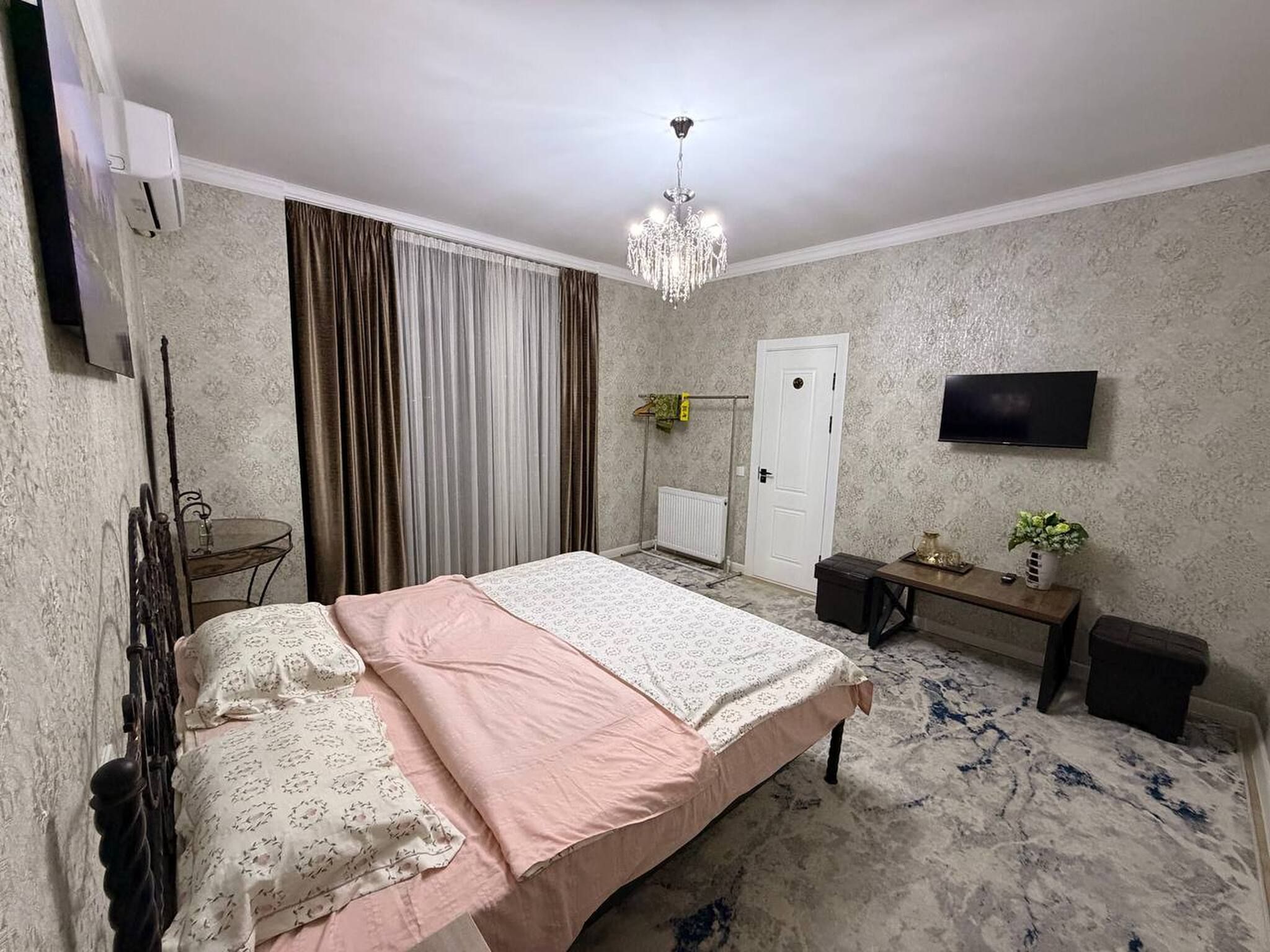 Une chambre à coucher comprenant un lit, un bureau, une chaise, un téléviseur et un lustre.